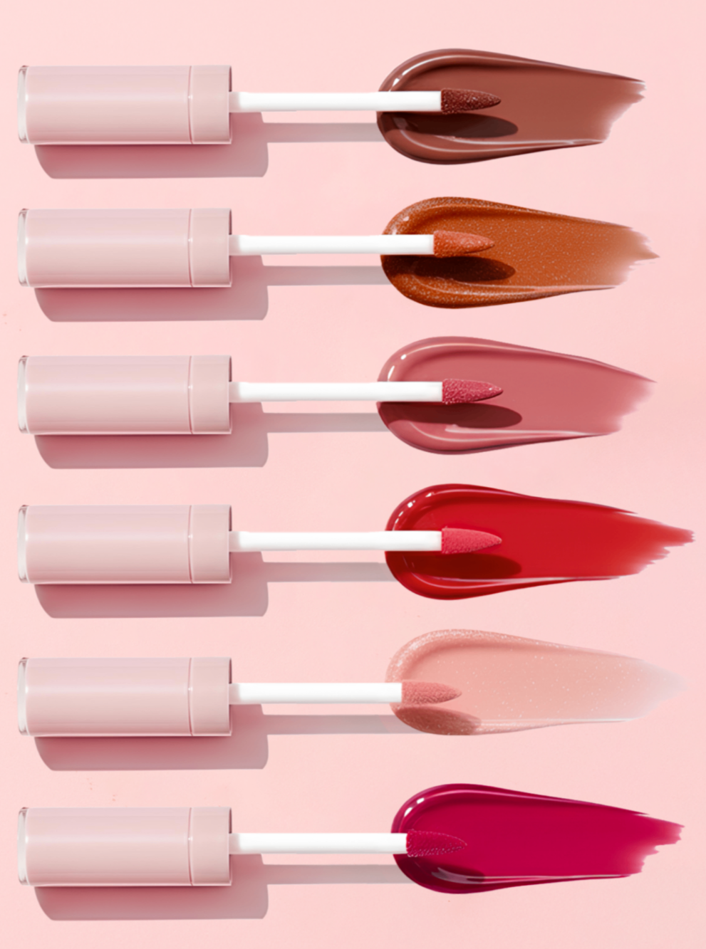 Set of lip gloss applicators with swatches on a pink background